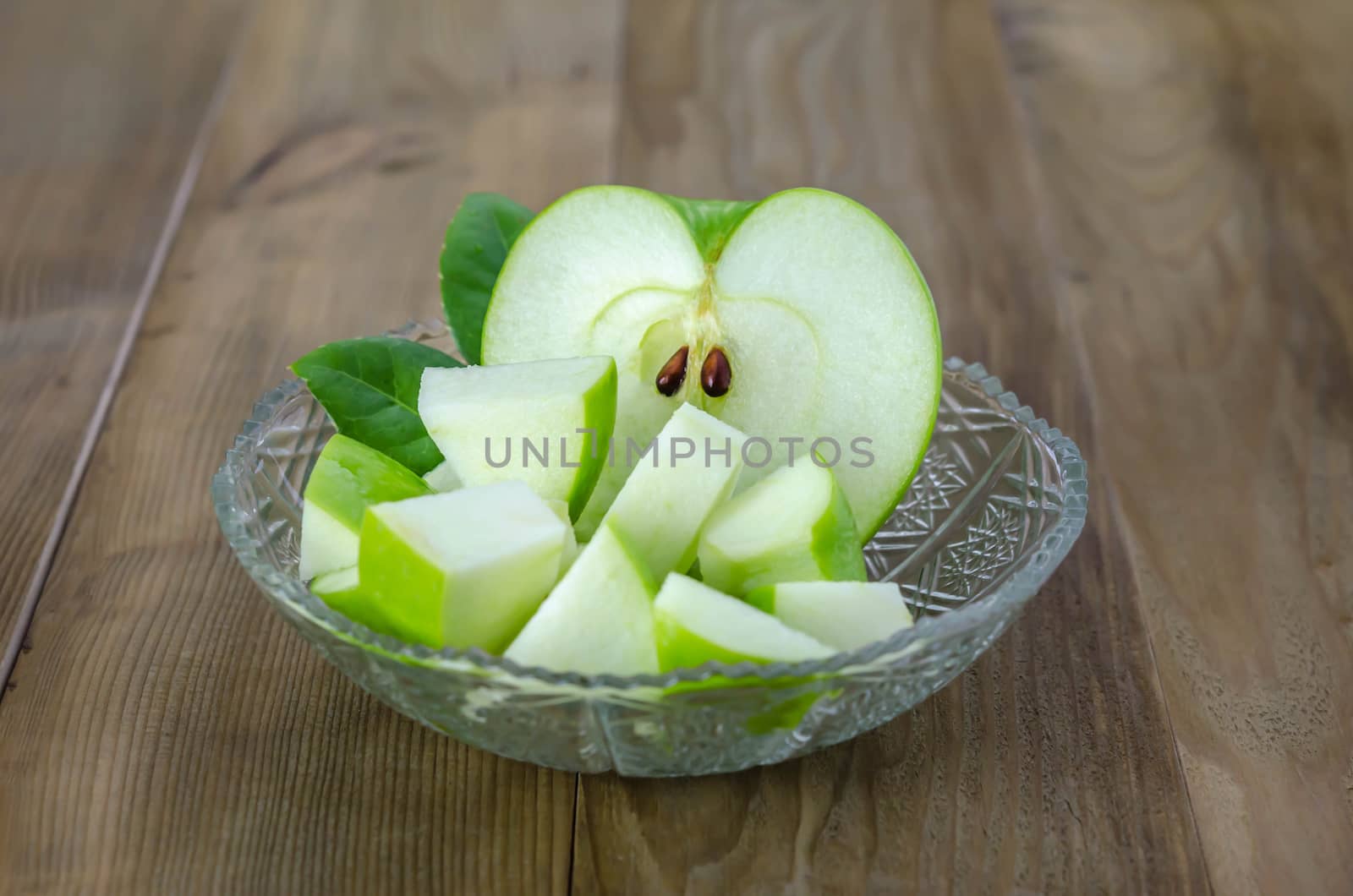 Ripe green apple with leaf and slice on a wooden background