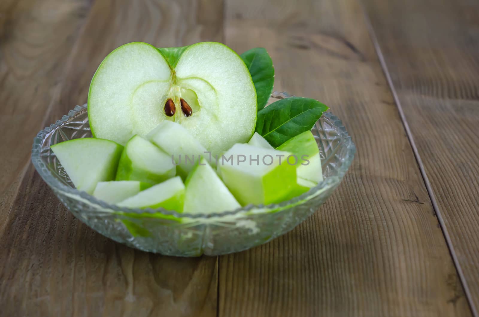 Ripe green apple with leaf and slice on a wooden background