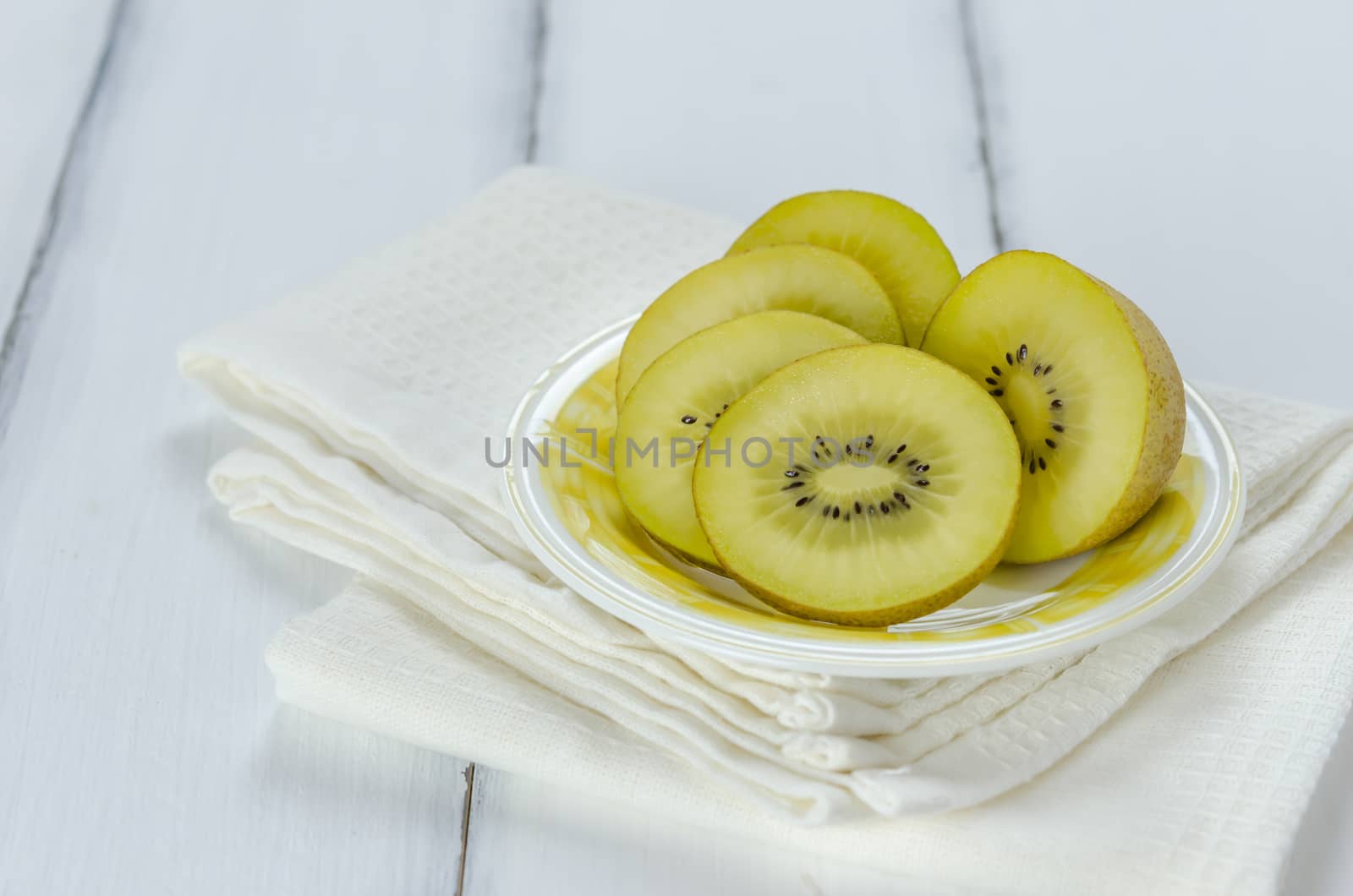 golden kiwi fruit and sliced on dish over white wooden background
