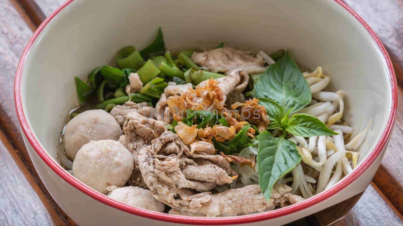Asian white noodles with pork and vegetables in bowl over wooden background