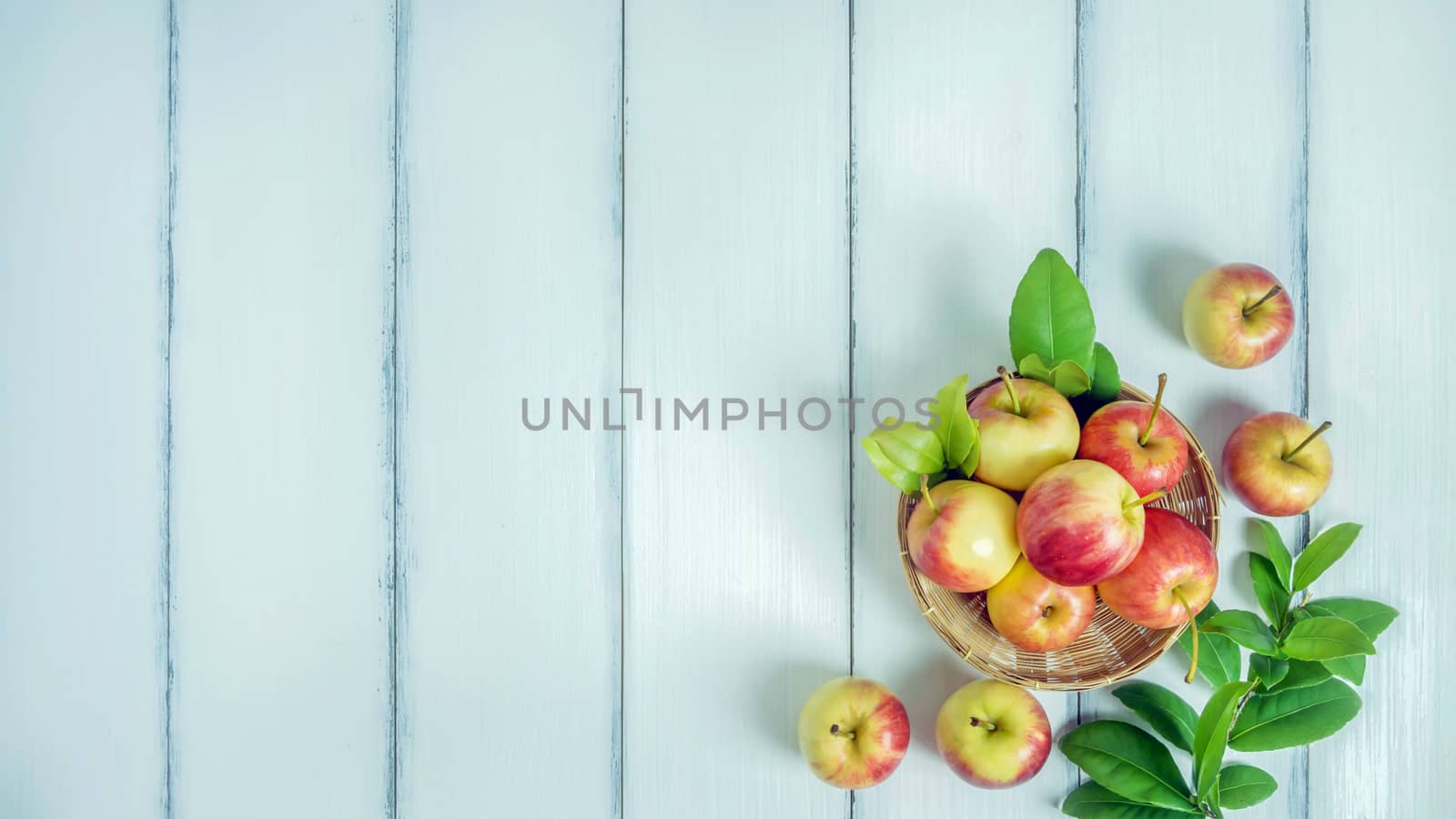 Top view red and yellow apple with leaves and  bamboo basket on  white wooden background with free space for text