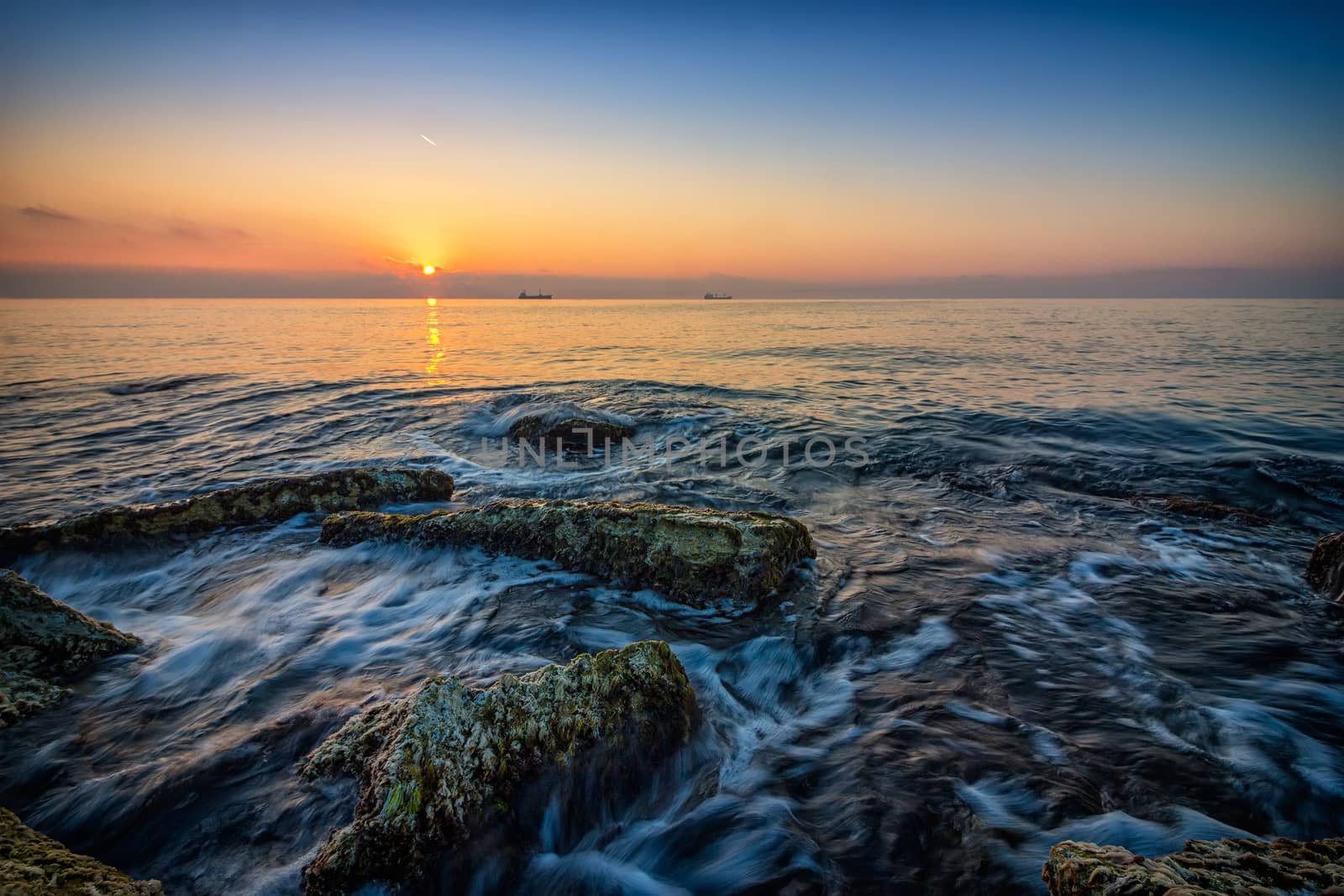 Sea sunrise. Beauty sea rocky beach with slow shutter and waves flowing out.