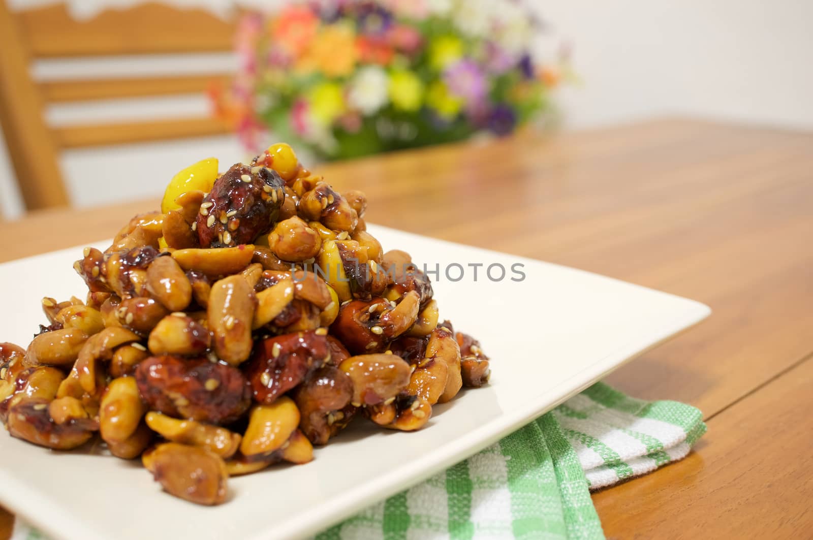 Fried chinese jujube and cashew nut vegetarian include gingko and nut with sesame on white plate with green fabric on wood table and blur flower as background.