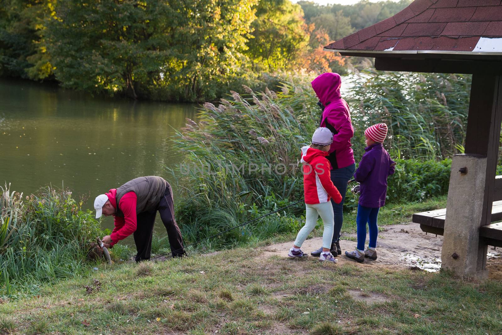 A family of four people on the lake fishing. Caught pike. Fishing. Dad caught a fish, little girls are happy. Autumn. by AndrewBu