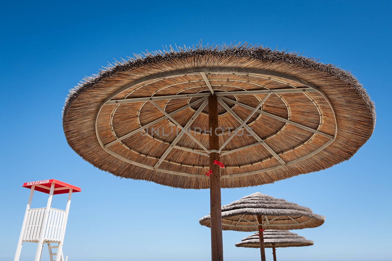 Life guard stand and three beach umbrellas on a blue sky background