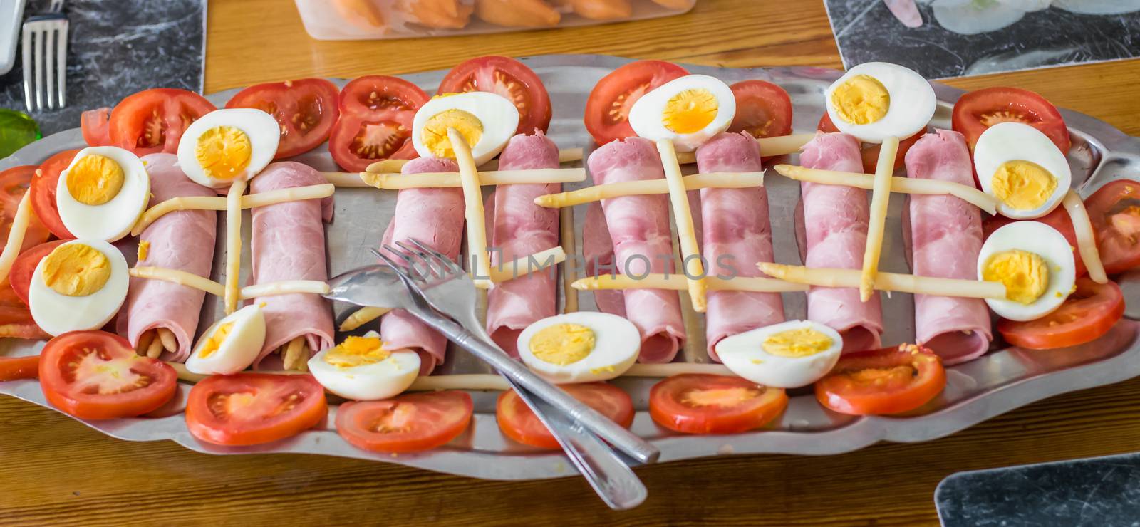 half boiled eggs, sliced tomatoes, ham and asparagus in a metal tray. French food