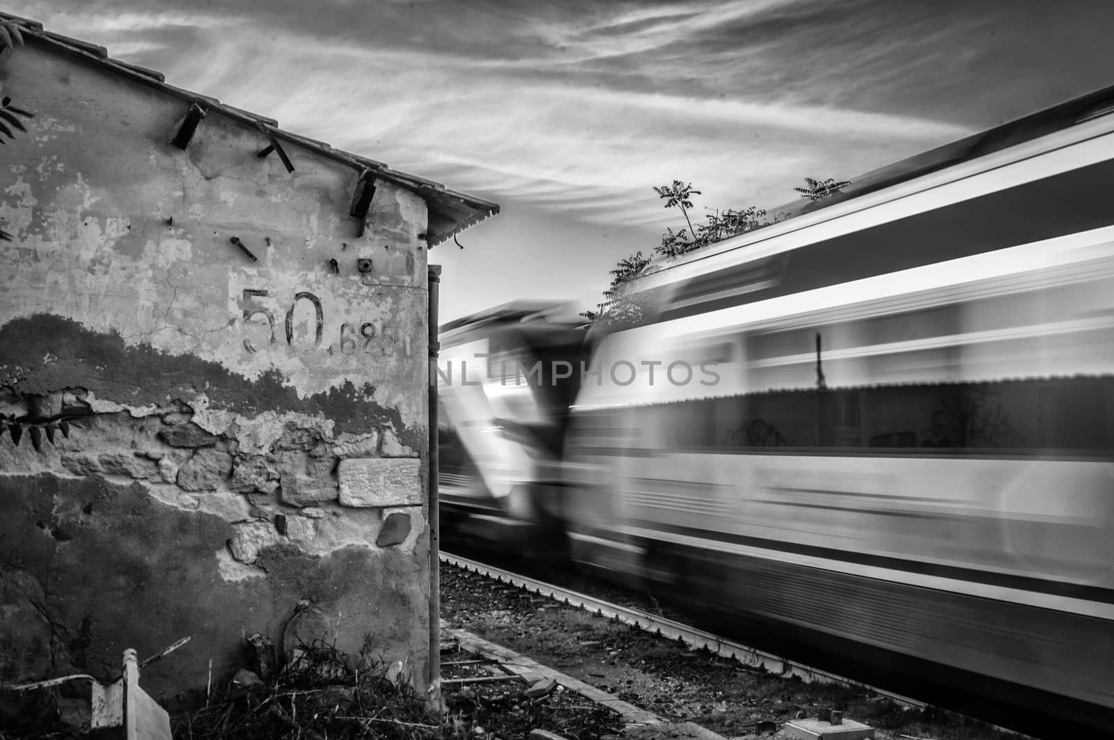 Train running near an abandoned rural rail station in black and white