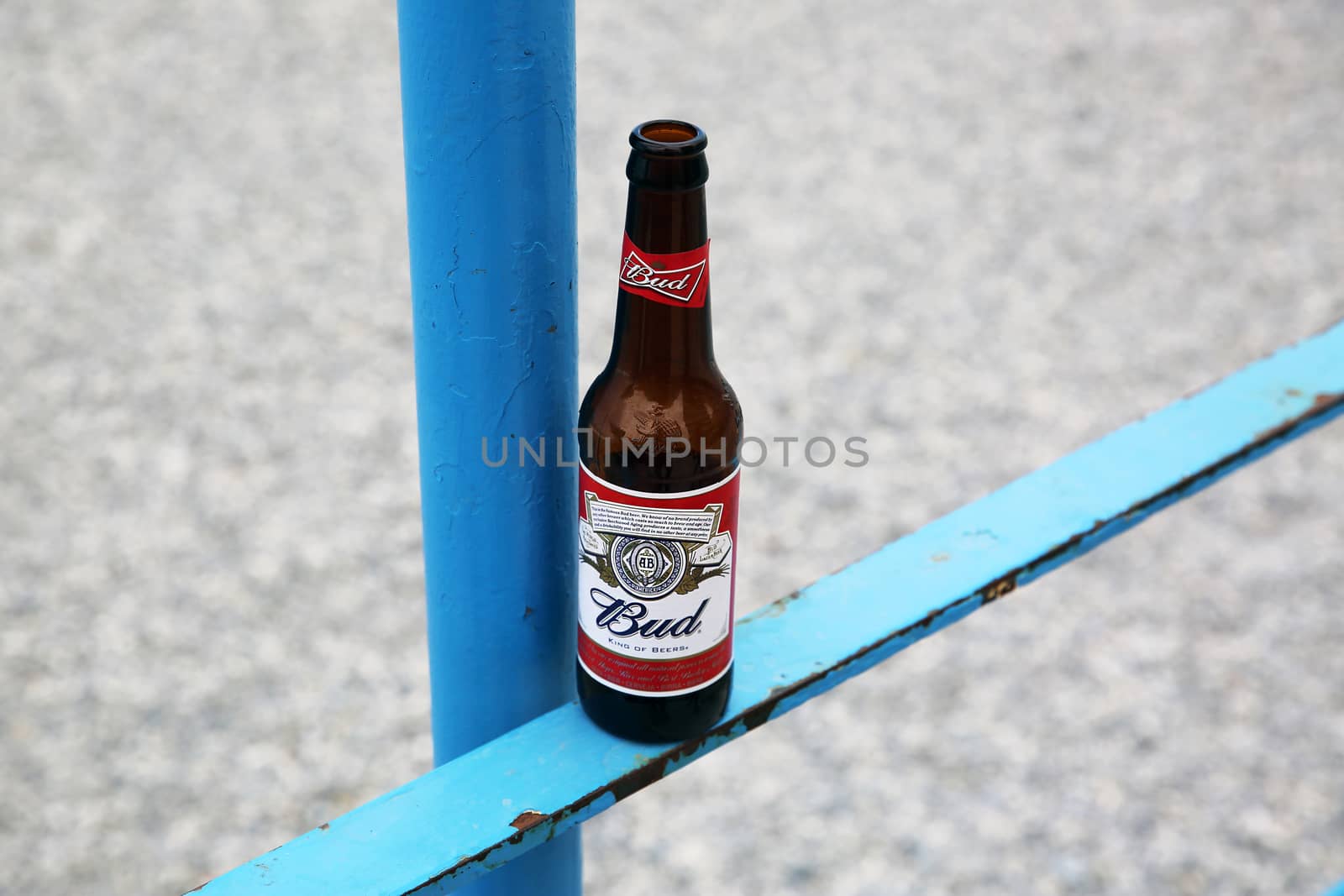 Menton, France - May 14, 2016: Bottle of Budweiser Beer on a Blue Metal Fence, Beach in the Background