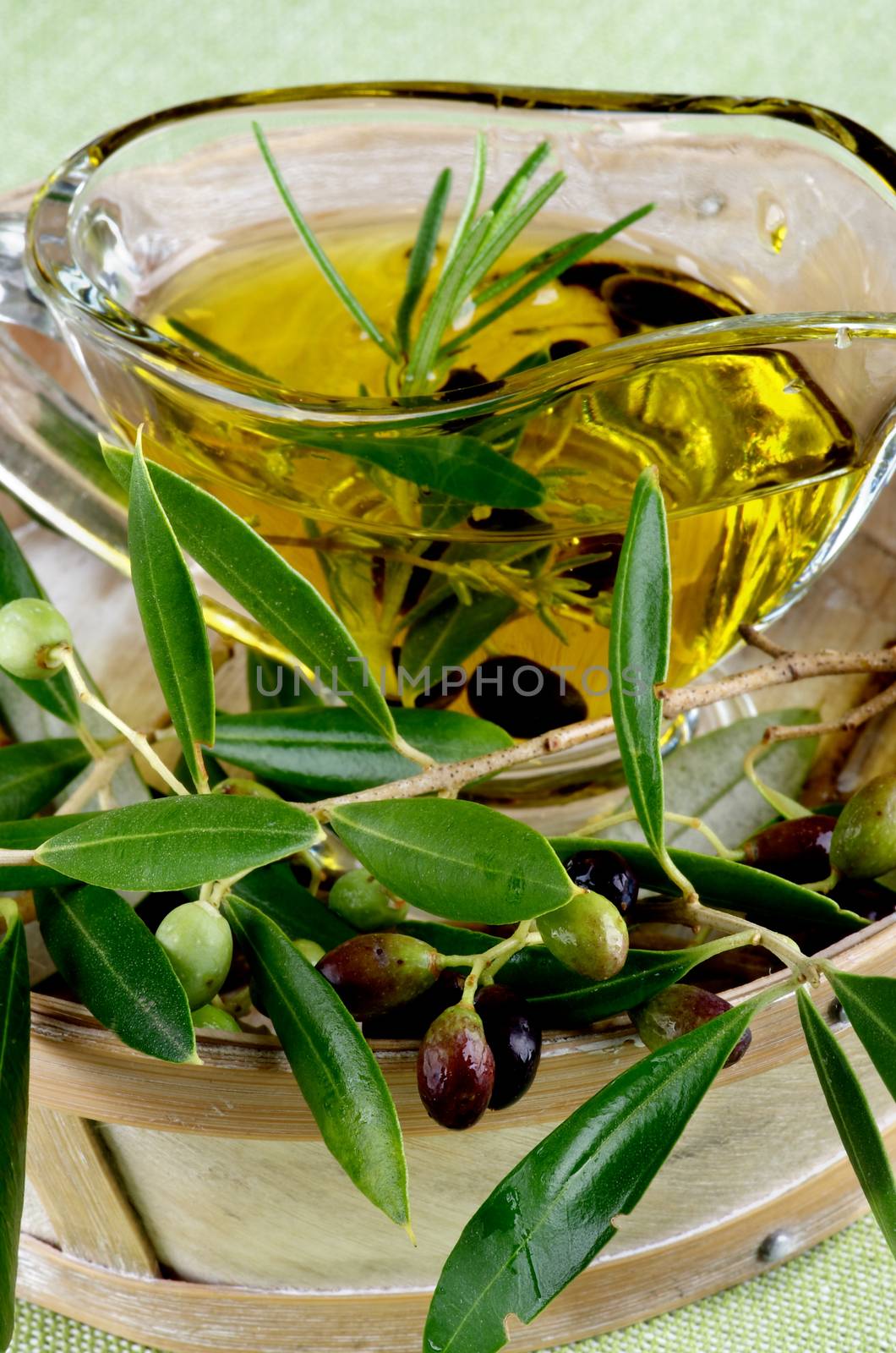 Raw Green and Black Olives with Leafs with Olive Oil in Glass Gravy in Wooden Bowl closeup on Green Textile background