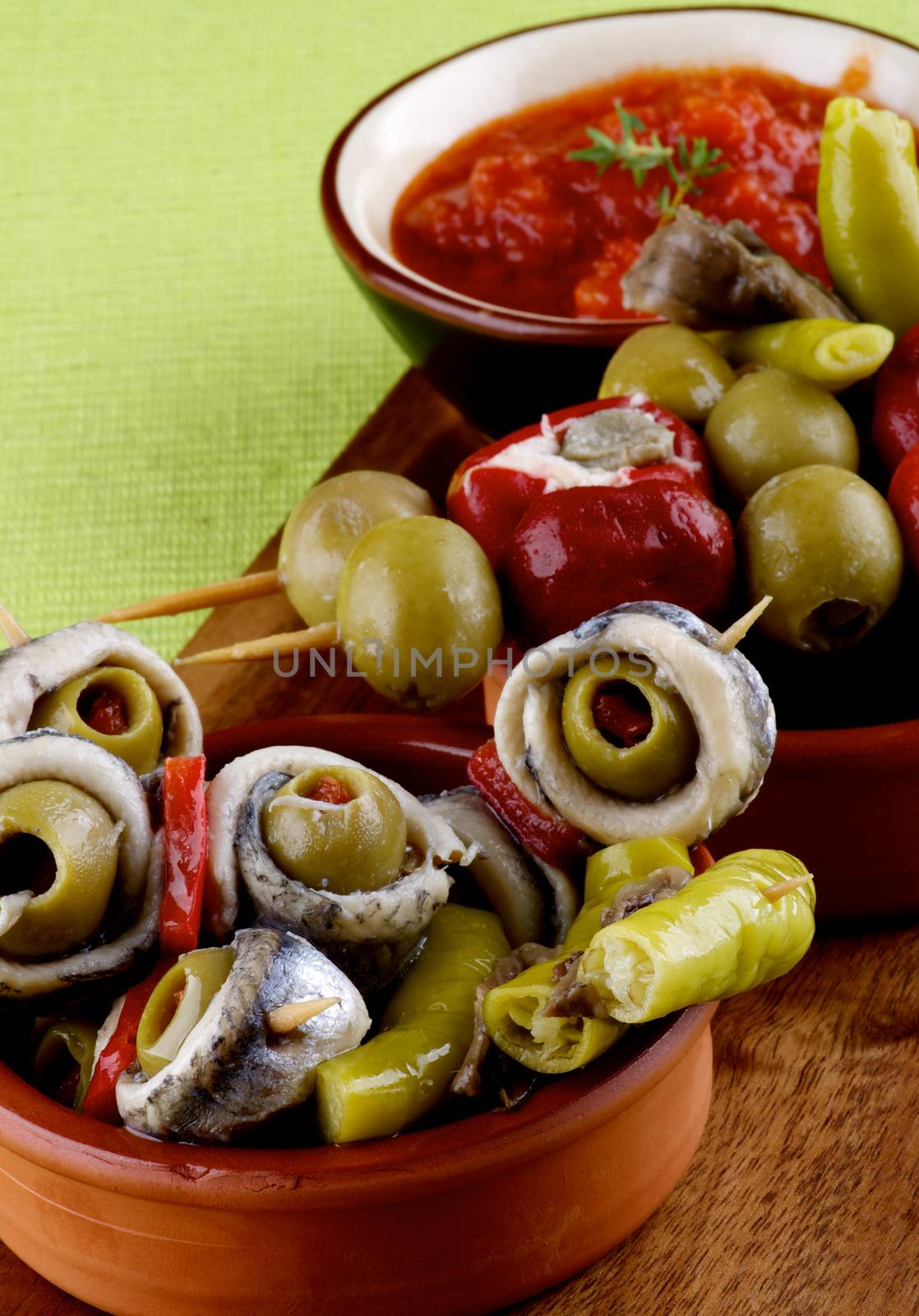 Delicious Spanish Snacks with Anchovies, Green Olives, Small Peppers Stuffed with Cheese and Tomatoes Sauce in Various Bowls closeup on Green Napkin. Focus on Foreground
