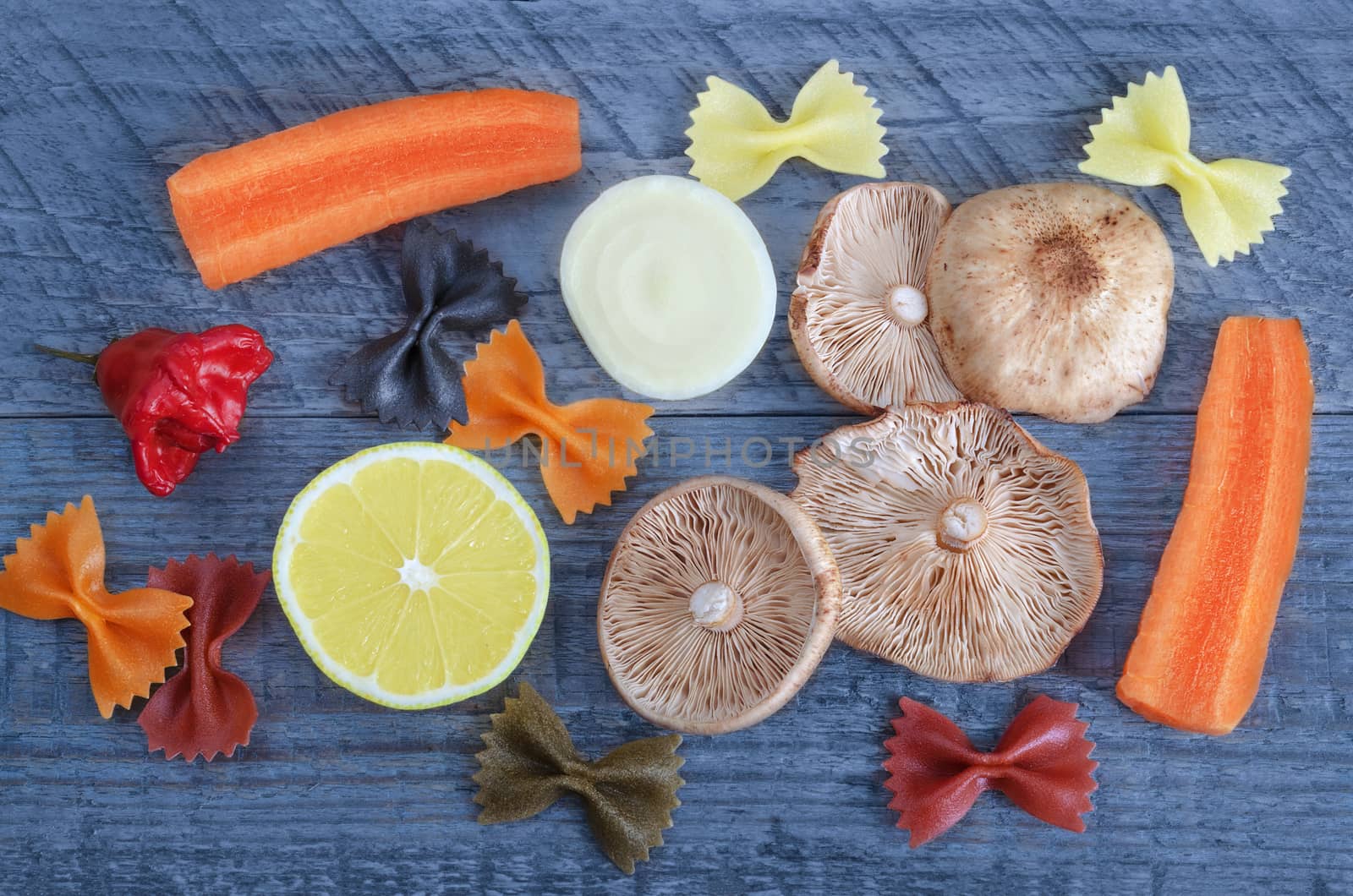 Mushrooms, vegetables and pasta are on a blue wooden background by Gaina