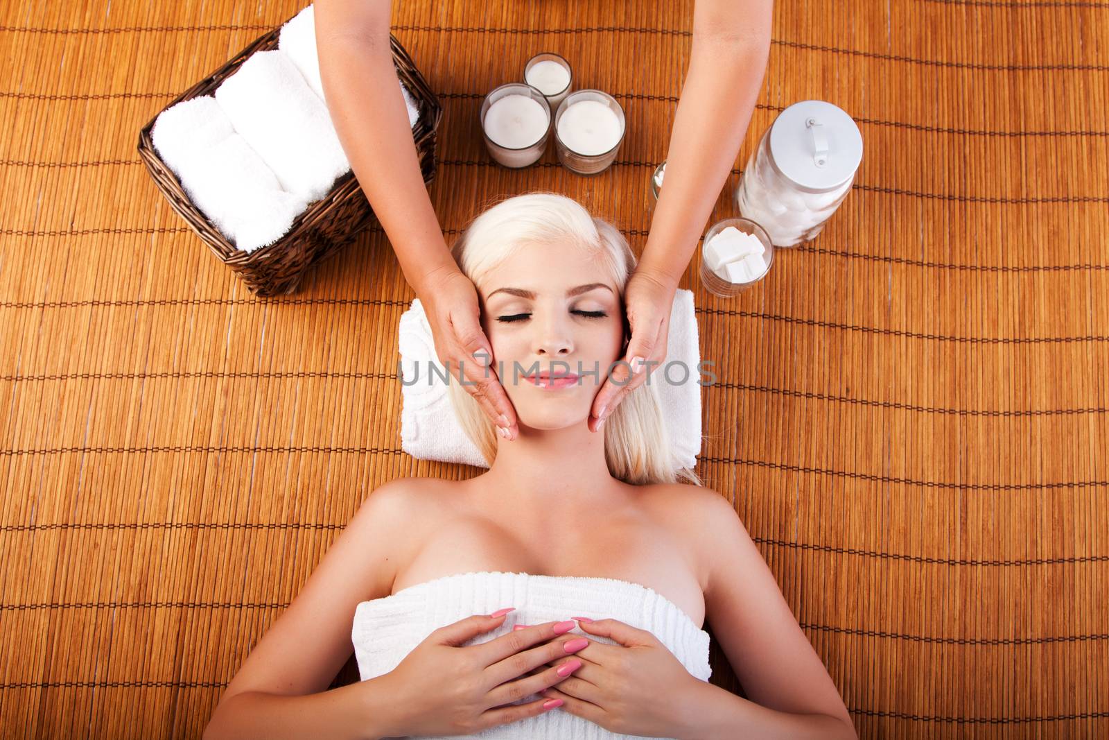 Beautiful young woman relaxing at spa getting therapeutic pampering facial massage, laying on bamboo.