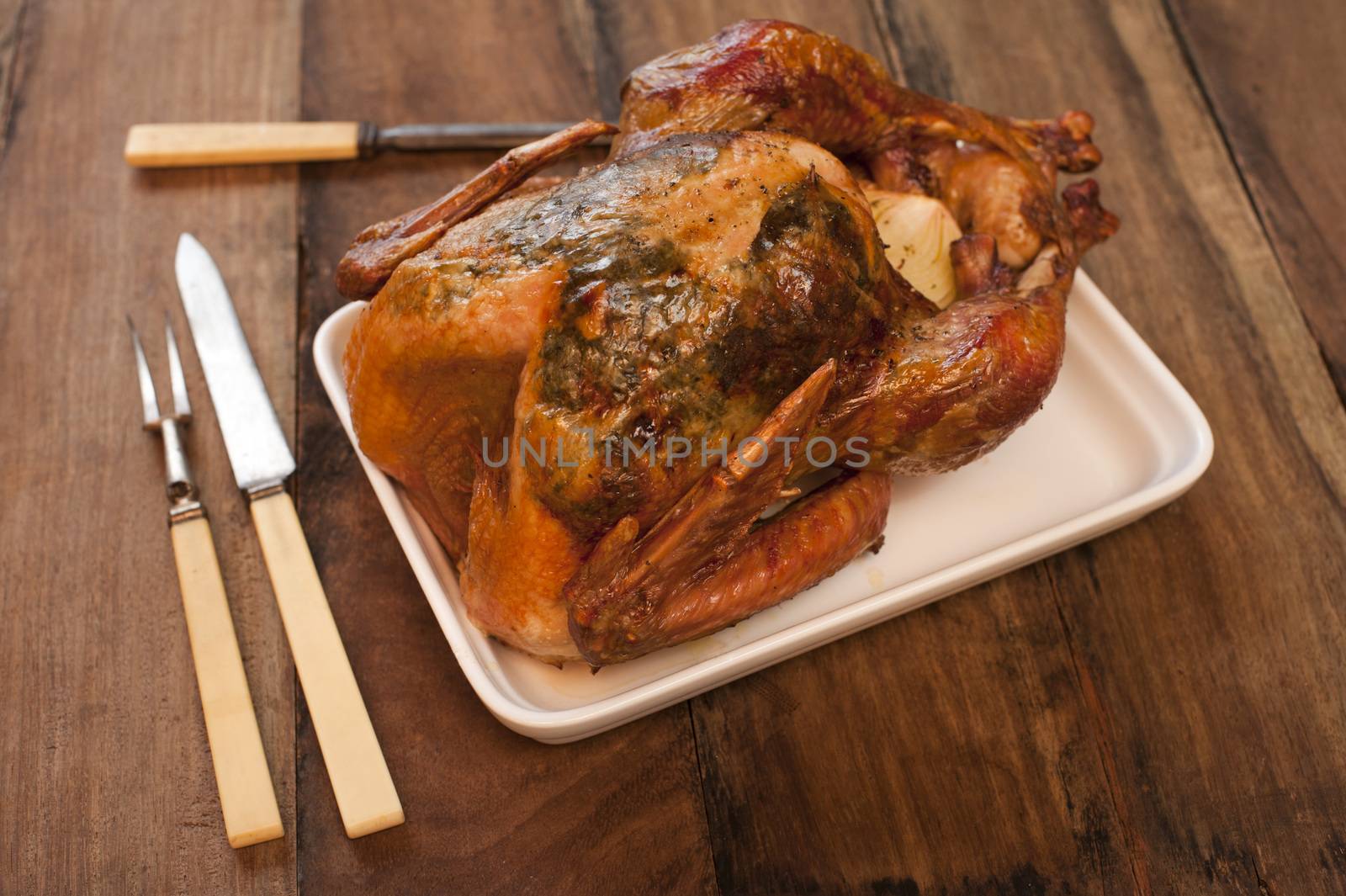 Roast chicken on a rectangular plate with a set of carving knife and fork on a wooden table waiting to be carved for dinner