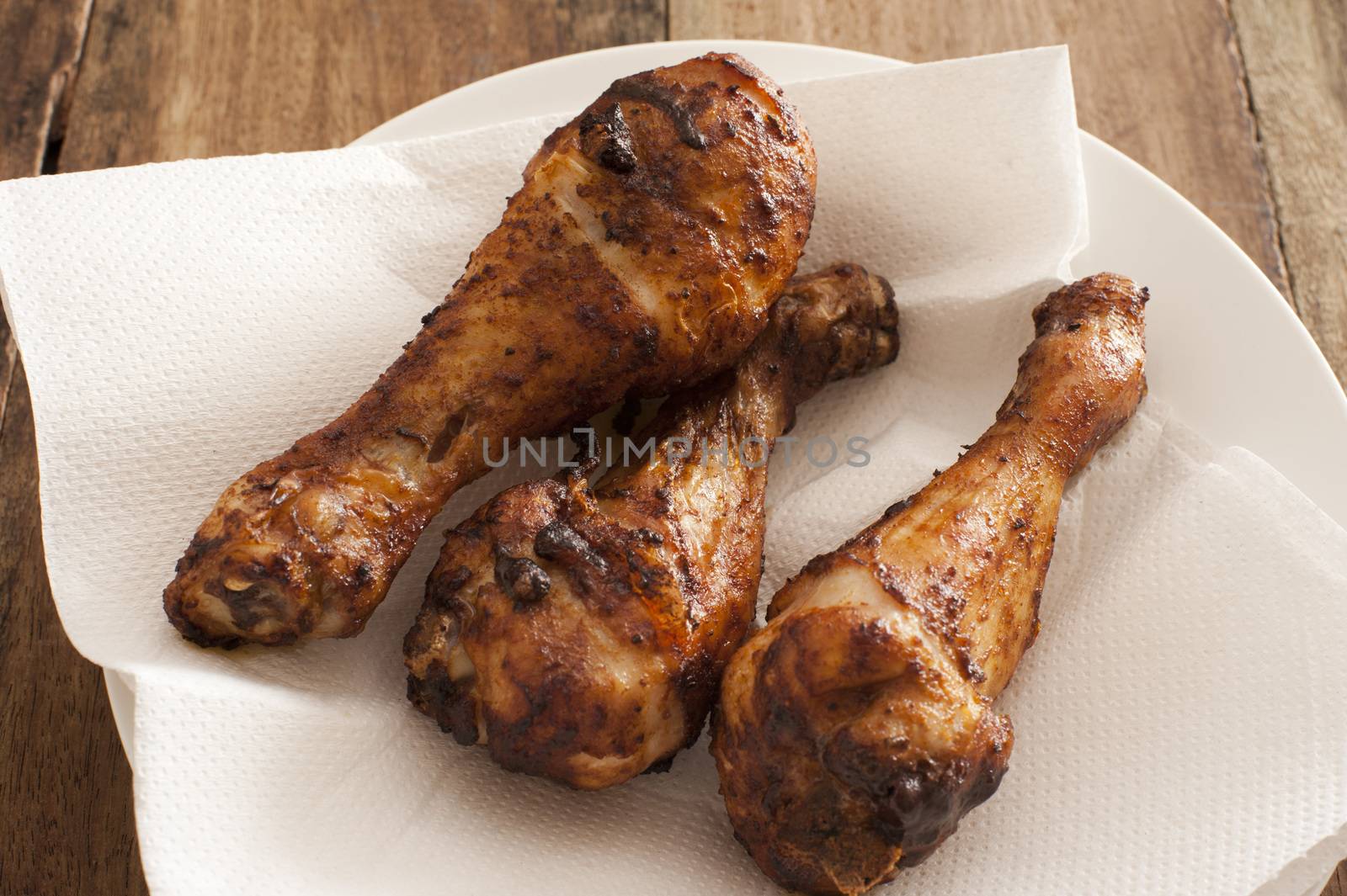 Three marinated spicy chicken drum sticks served on white paper on a plate for a delicious finger snack