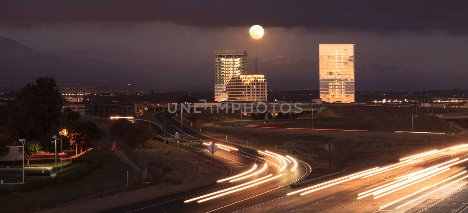 Full moon over a California highway with headlight trails near at sunset.