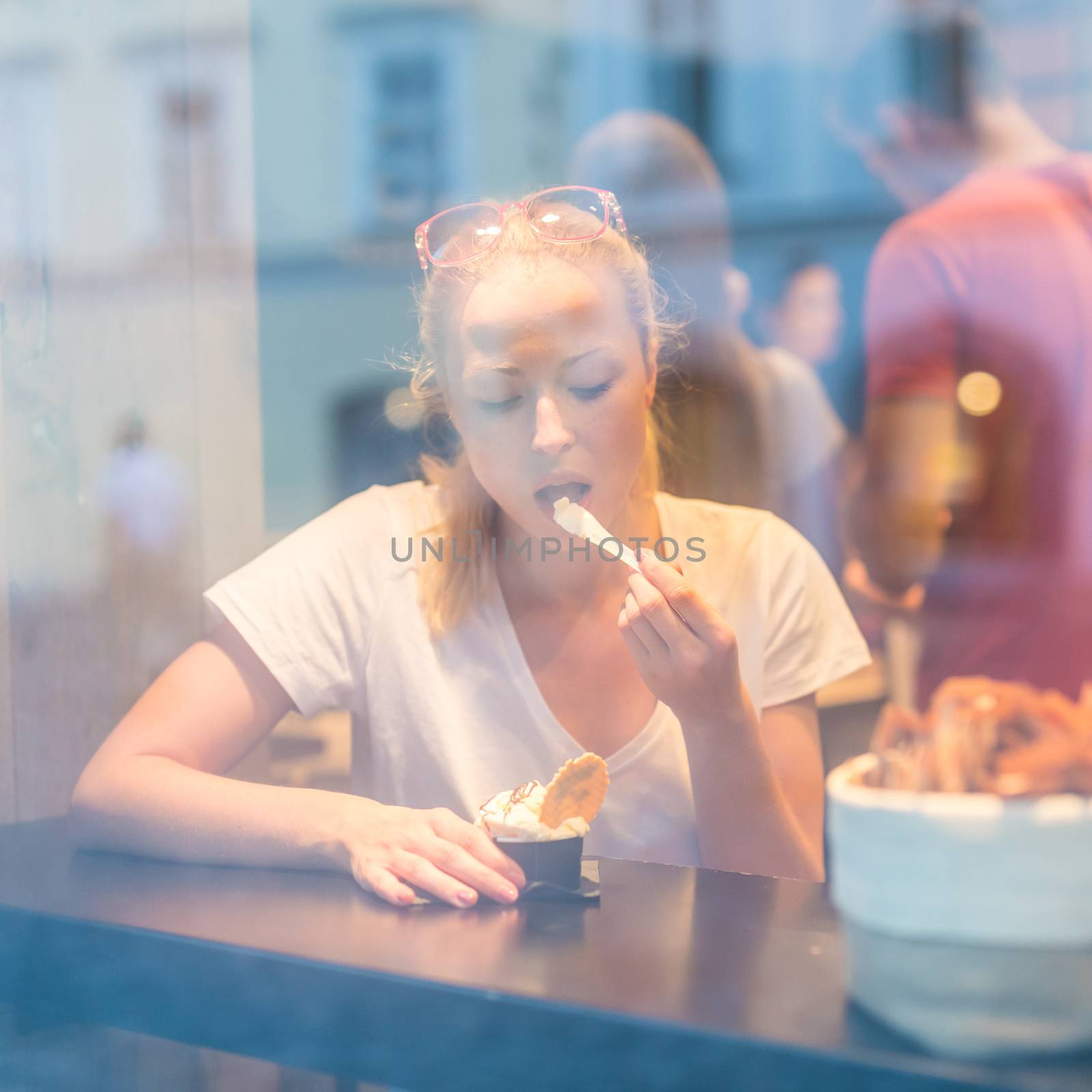 Young pretty woman eating icecream in gelateria. by kasto