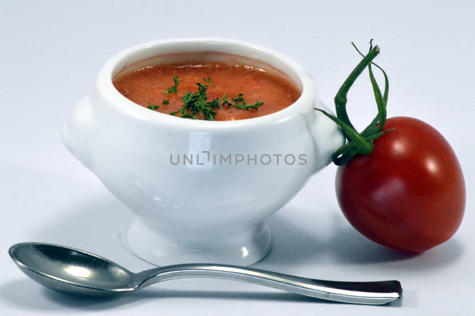 Cream of tomato soup in a white bowl with a spoon and a cherry tomato.