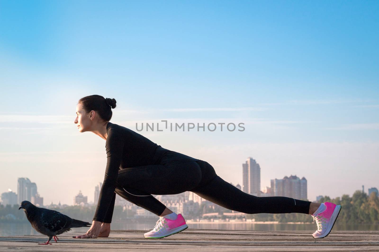 Young pretty fitness woman exercises on pier during morning sport training workout