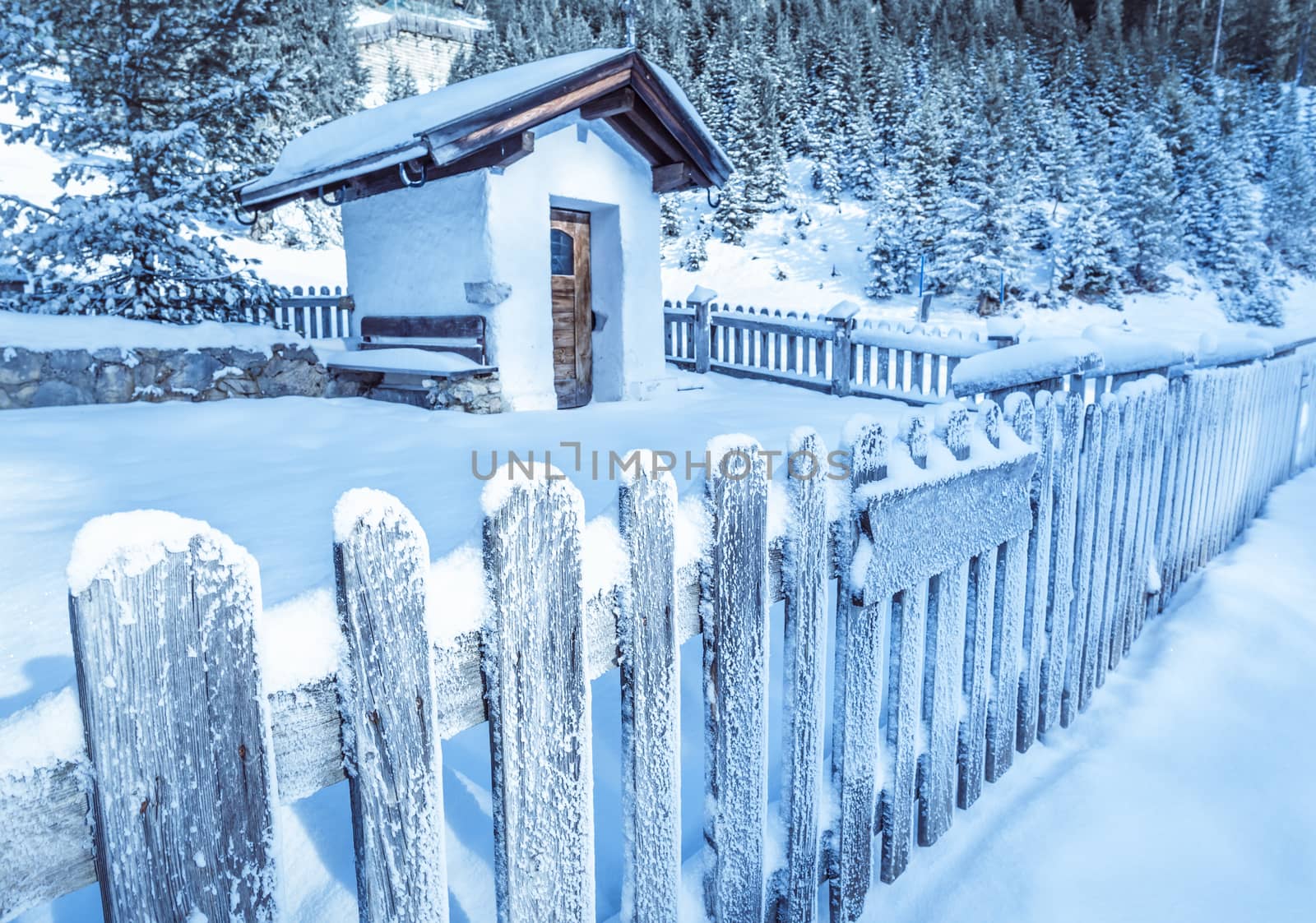 Winter idyllic scenery with an old wooden fence covered by snow, which surrounds a rustic alpine chapel, in the Austrian Alps. Image taken in Ehrwald, Austria.