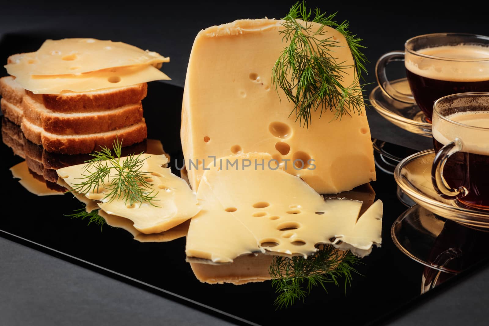 Cheese with fennel, white loaf and two cups of coffee on a black background with reflection