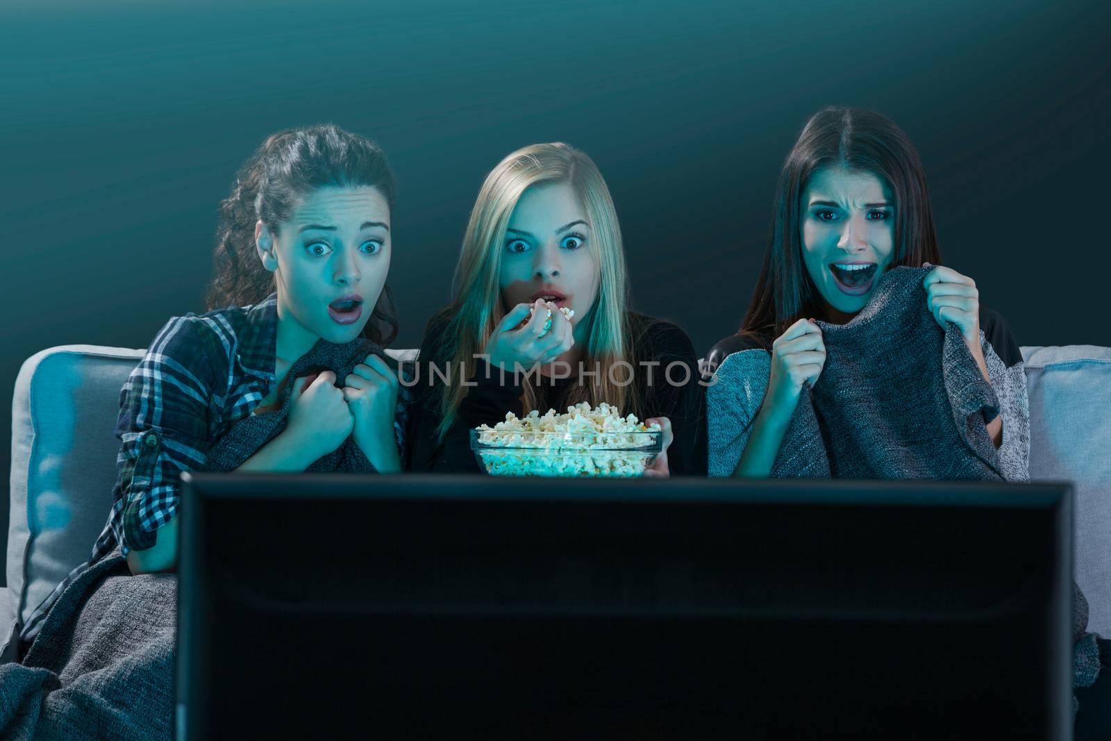 Teenage girls watching horror movie with popcorn