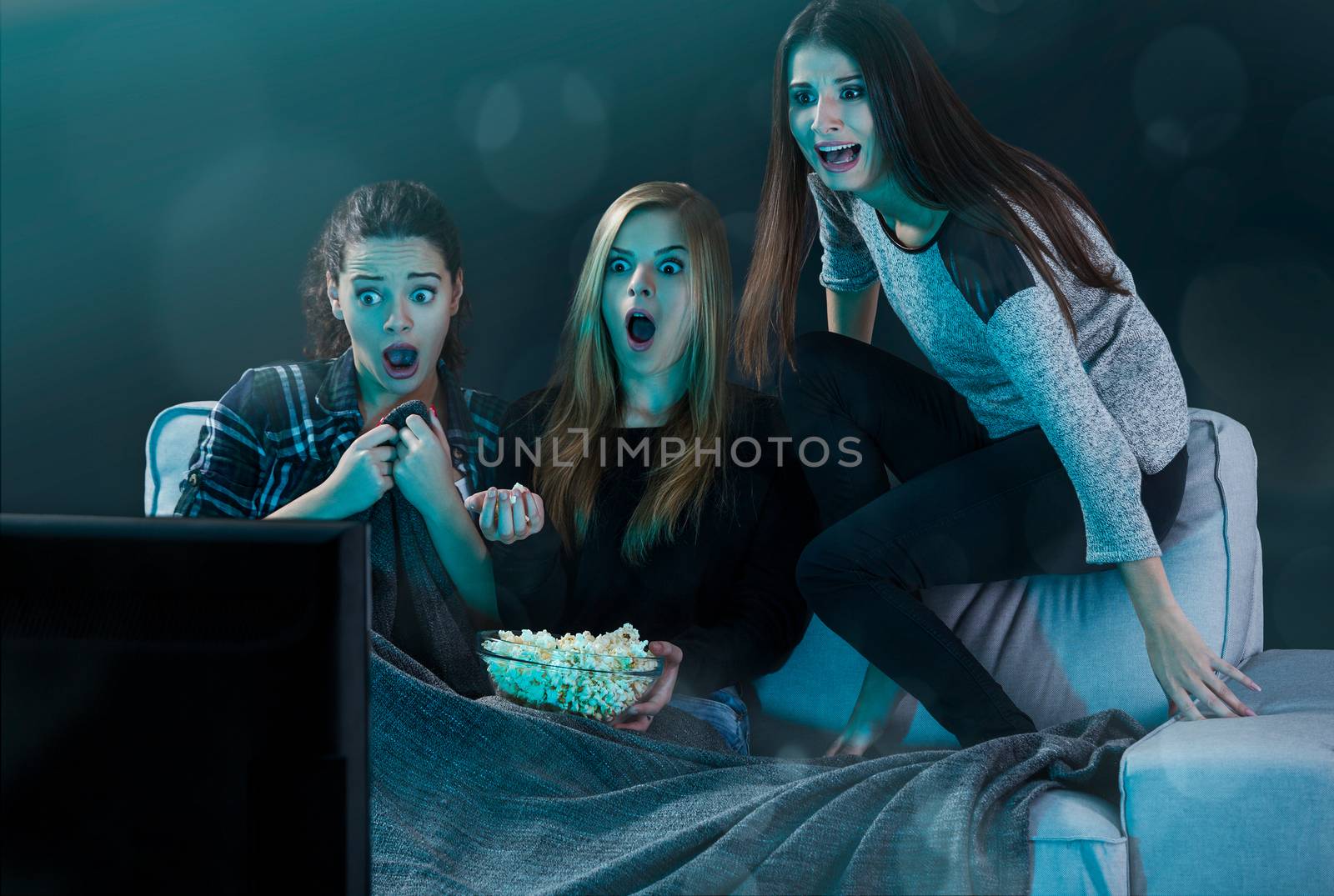 Teenage girls watching horror movie with popcorn
