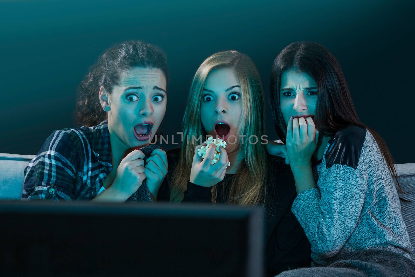 Teenage girls watching horror movie with popcorn