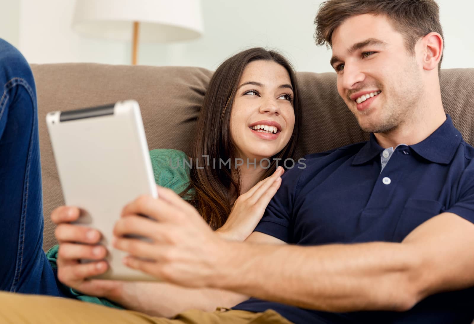 Young couple sitting on the sofa and watching something on a tablet