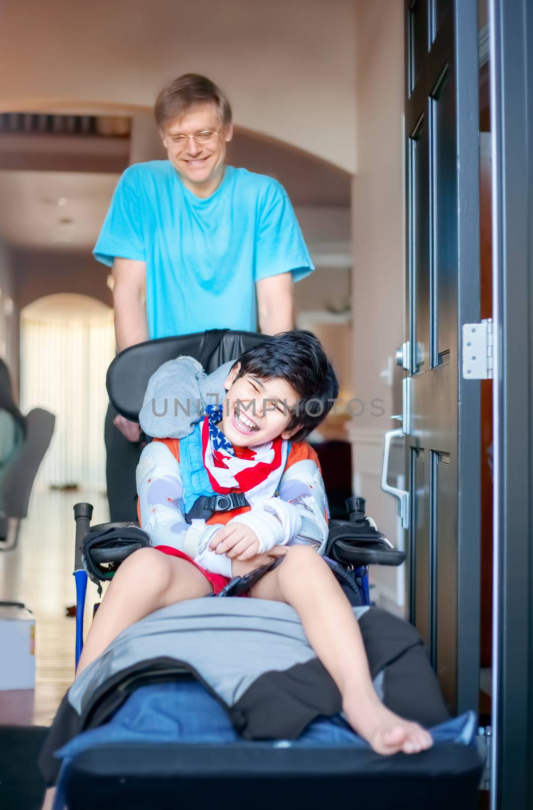 Father pushing disabled son in wheelchair out the front door by jarenwicklund