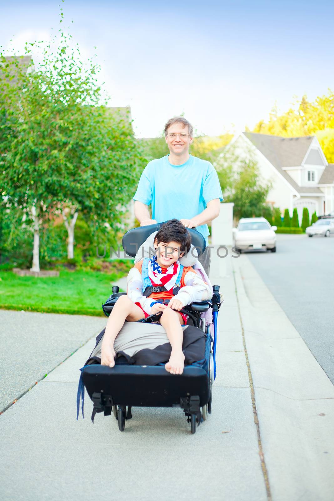 Father pushing ten year old  disabled son in wheelchair outdoors by jarenwicklund