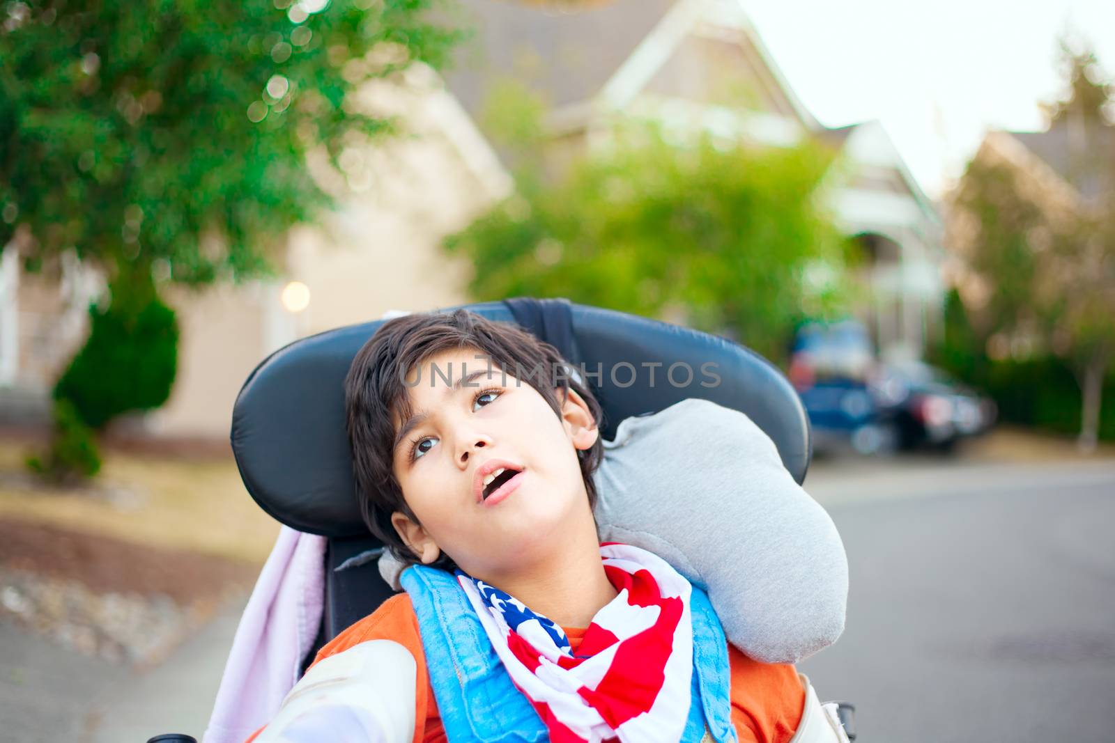 Disabled ten year old boy sitting in wheelchair outdoors looking up into sky, thinking