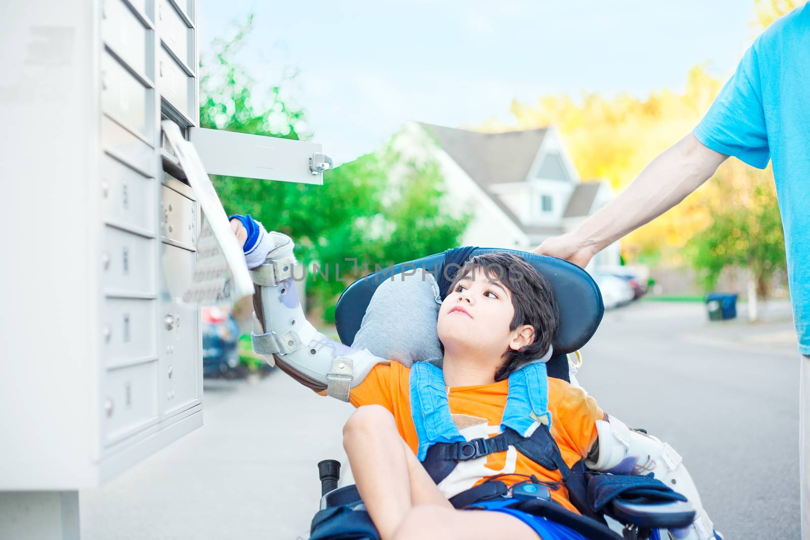 Disabled ten year old boy in wheelchair reaching up to get mail from mailbox outdoors