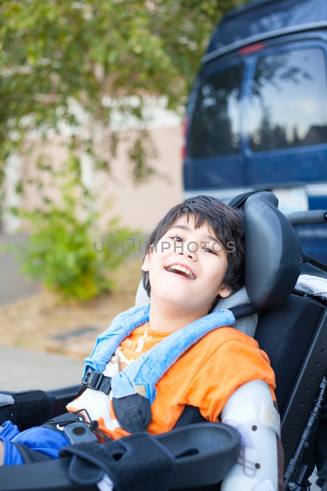 Biracial ten year old boy sitting in wheelchair outdoors smiling and relaxing
