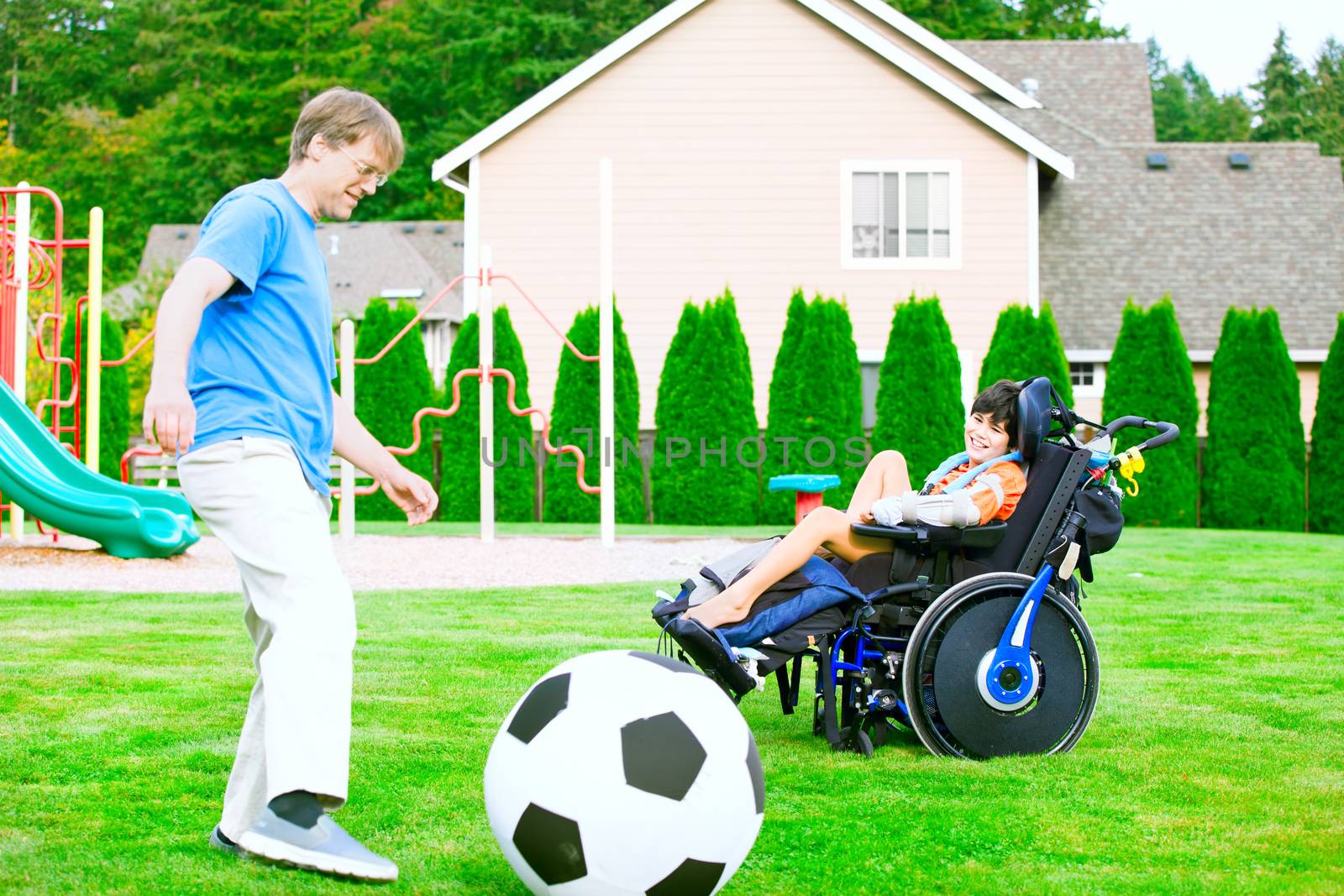 Caucasian father playing soccer with ten year old biracial disabled son in wheelchair at park outdoors