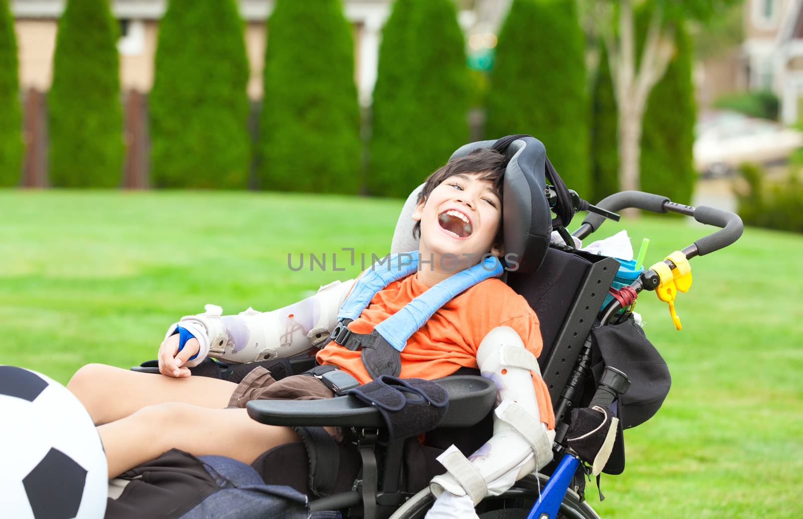 Ten year old biracial disabled boy in wheelchair playing with soccer ball at park