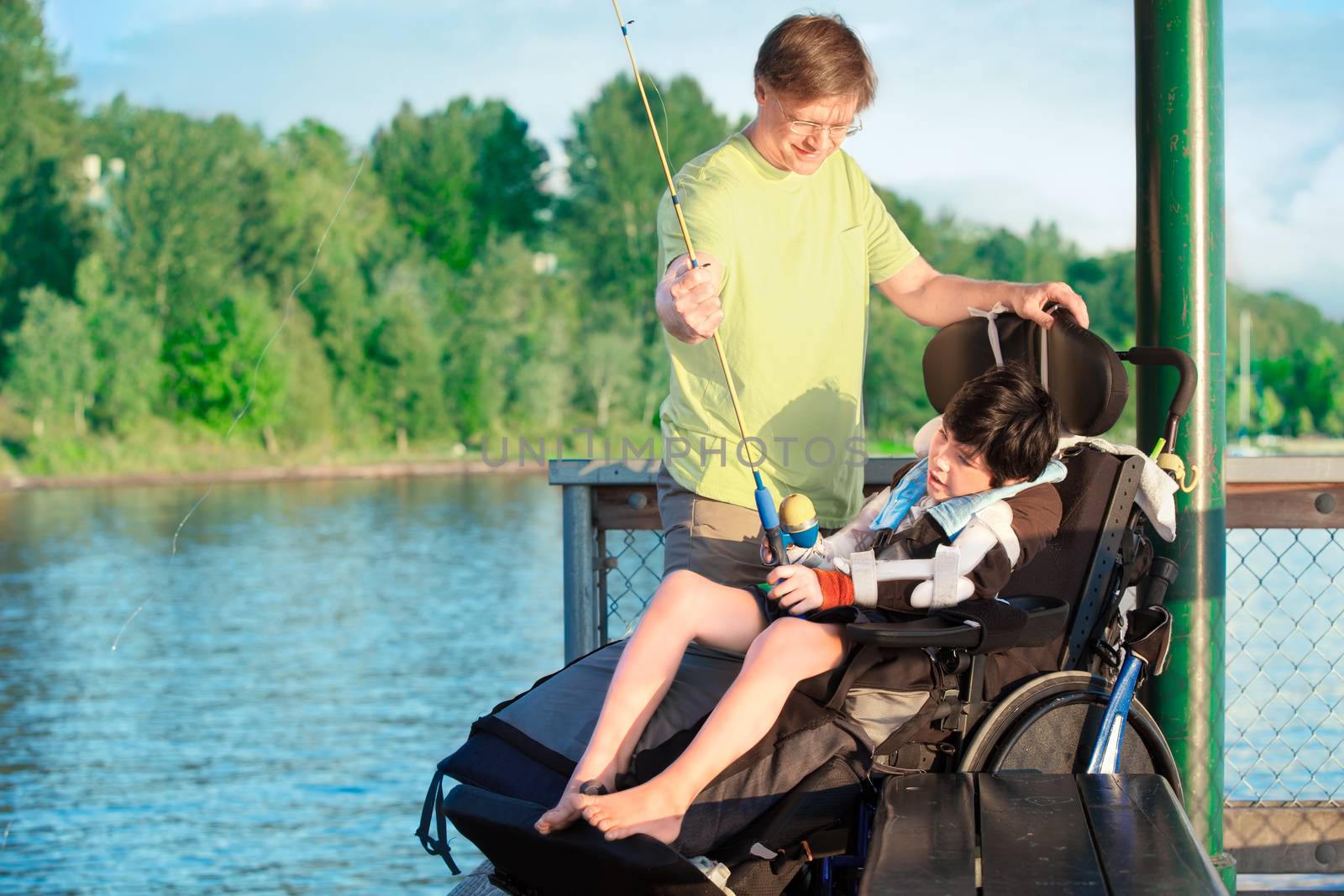 Caucasian father helping disabled ten year old son in wheelchair fish off pier