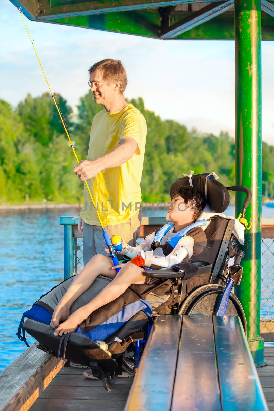 Father fishing off pier with disabled son in wheelchair by jarenwicklund