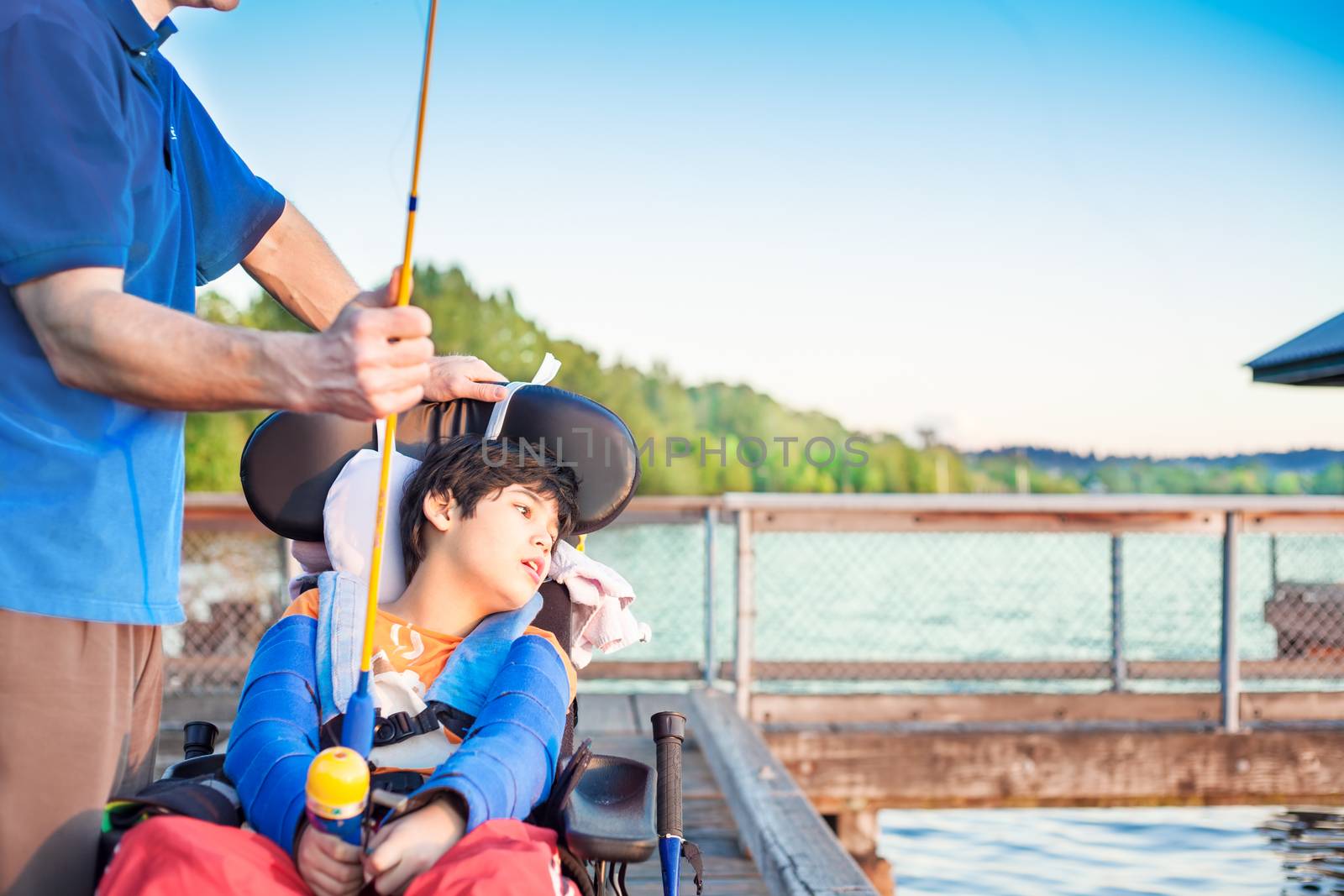 Caucasian father helping disabled ten year old son in wheelchair fish off pier