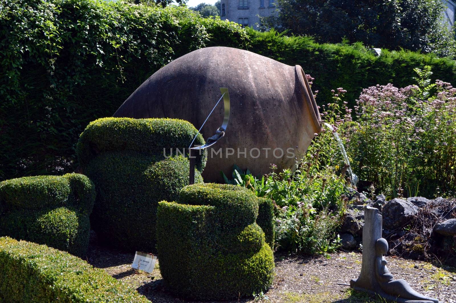 Enormous amphora serving as fountain in the middle of box tree and in the middle of a lawn.