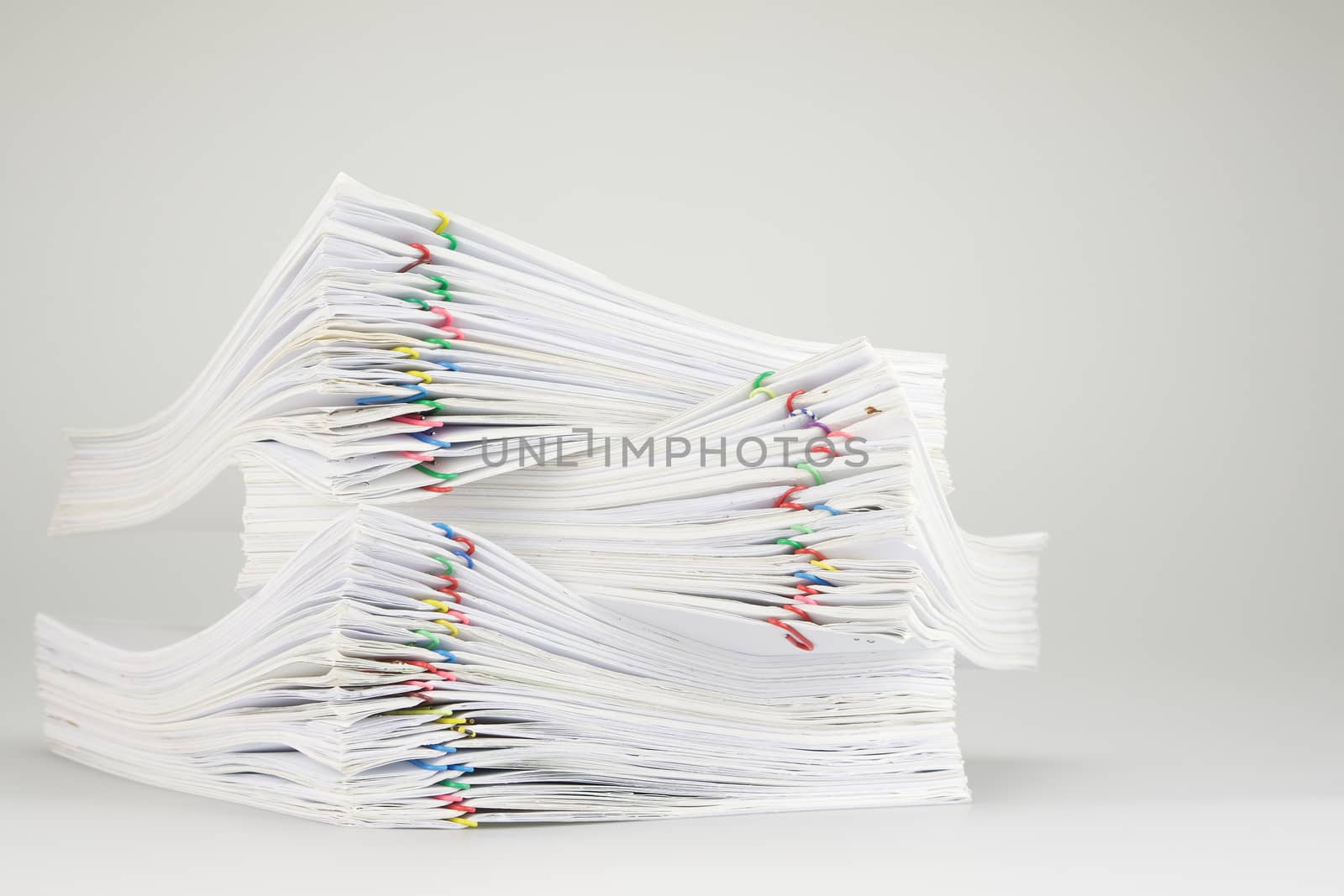 Pile overload of paperwork with colorful paper clip place on white table.