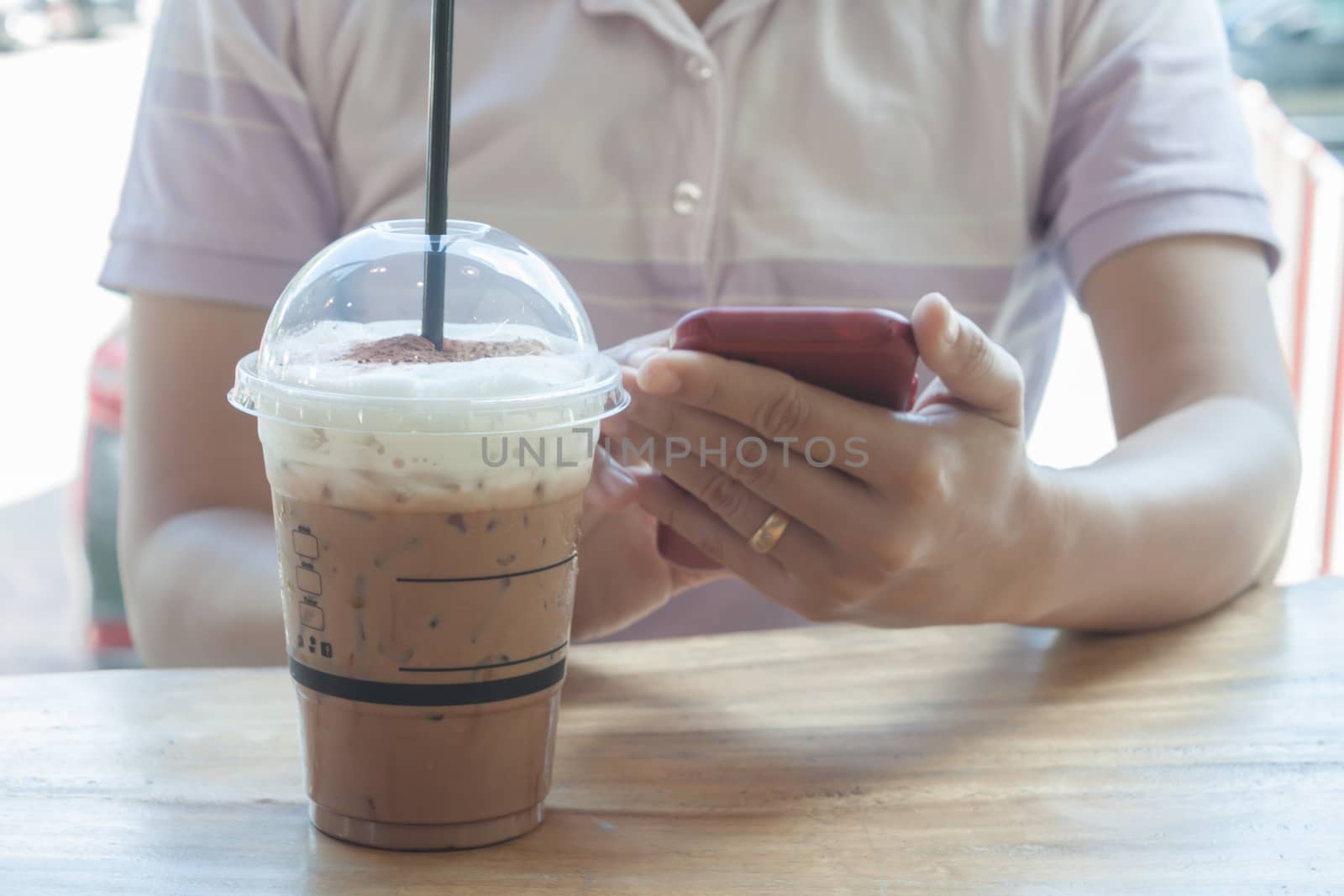 Woman hand holding phone with background of iced coffee, stock photo