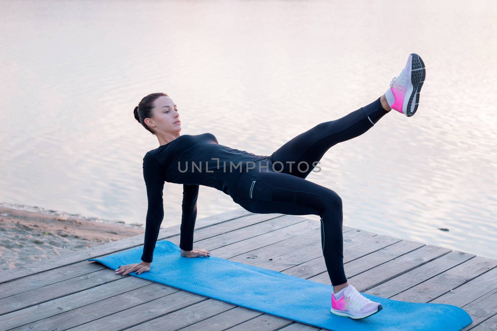 Young fitness woman exercises on pier during morning training workout by VeraVerano