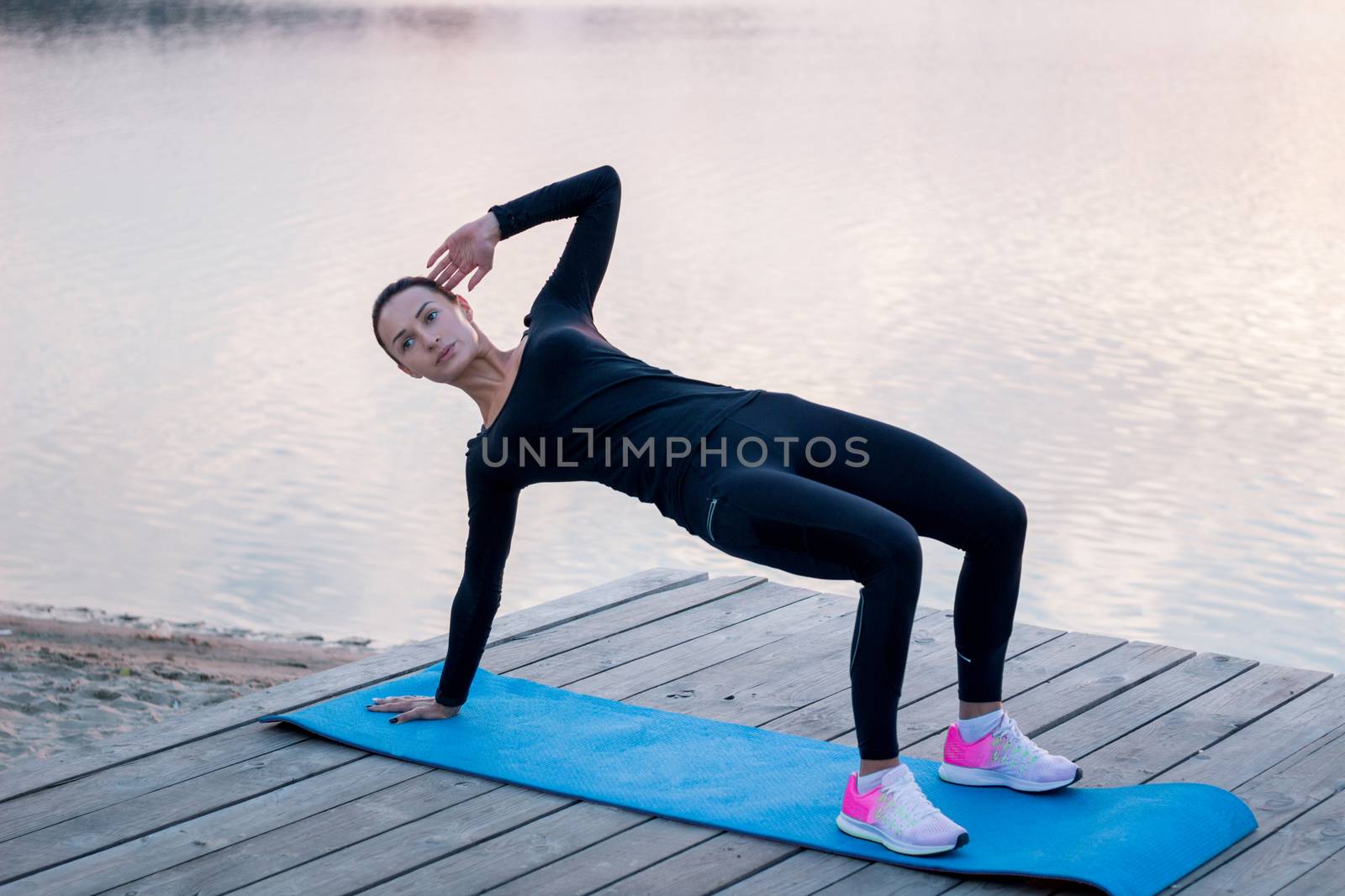 Young fitness woman exercises on pier during morning training by VeraVerano