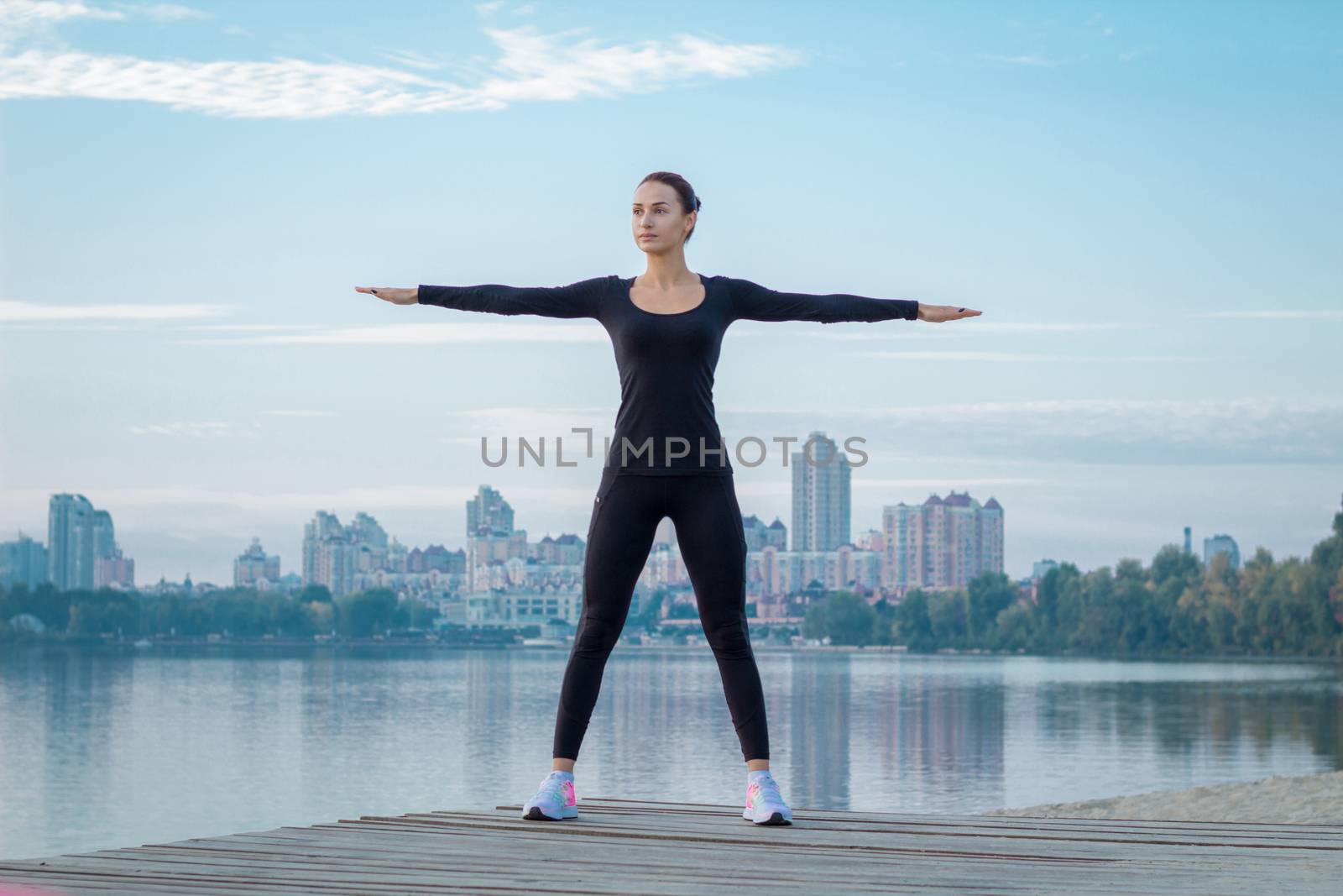 Young woman exercises on pier during morning fitness training workout by VeraVerano