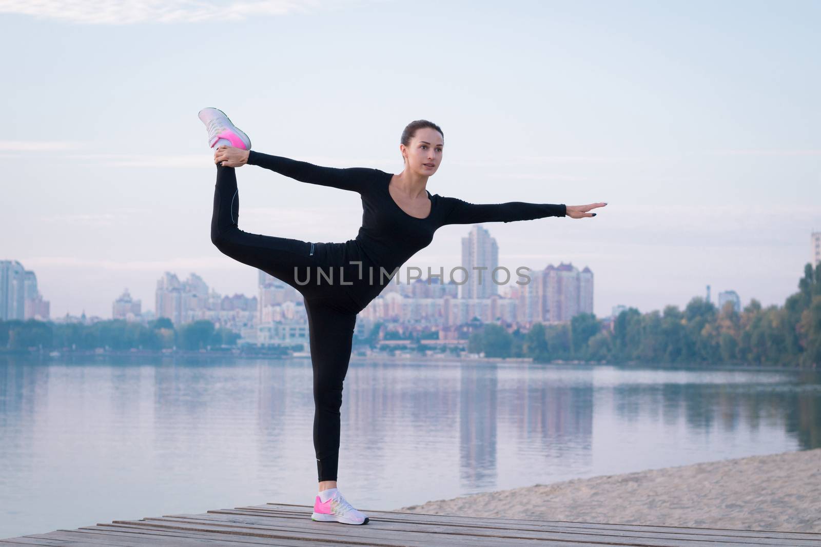 Young pretty fitness woman exercises on pier during morning training workout