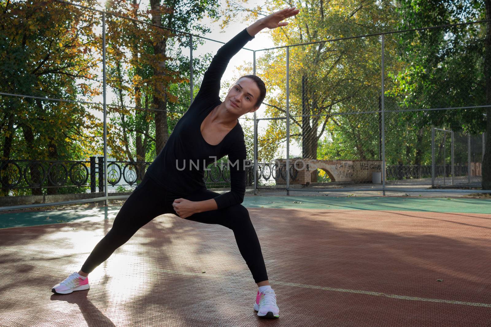 Young pretty fitness woman does stretching exercises during sport training workout on playground outdoor