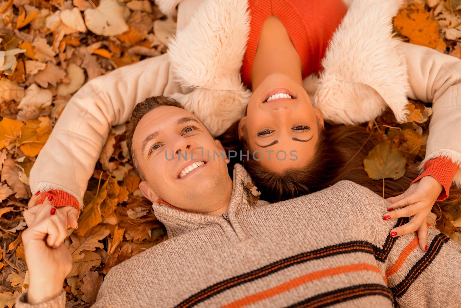 Beautiful smiling couple having fun in sunny forest in autumn colors. They are lying on the falls leaves. Close-up.