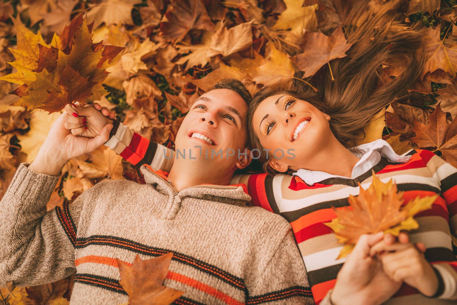 Beautiful smiling couple enjoying in sunny forest in autumn colors. They are lying on the falls leaves.