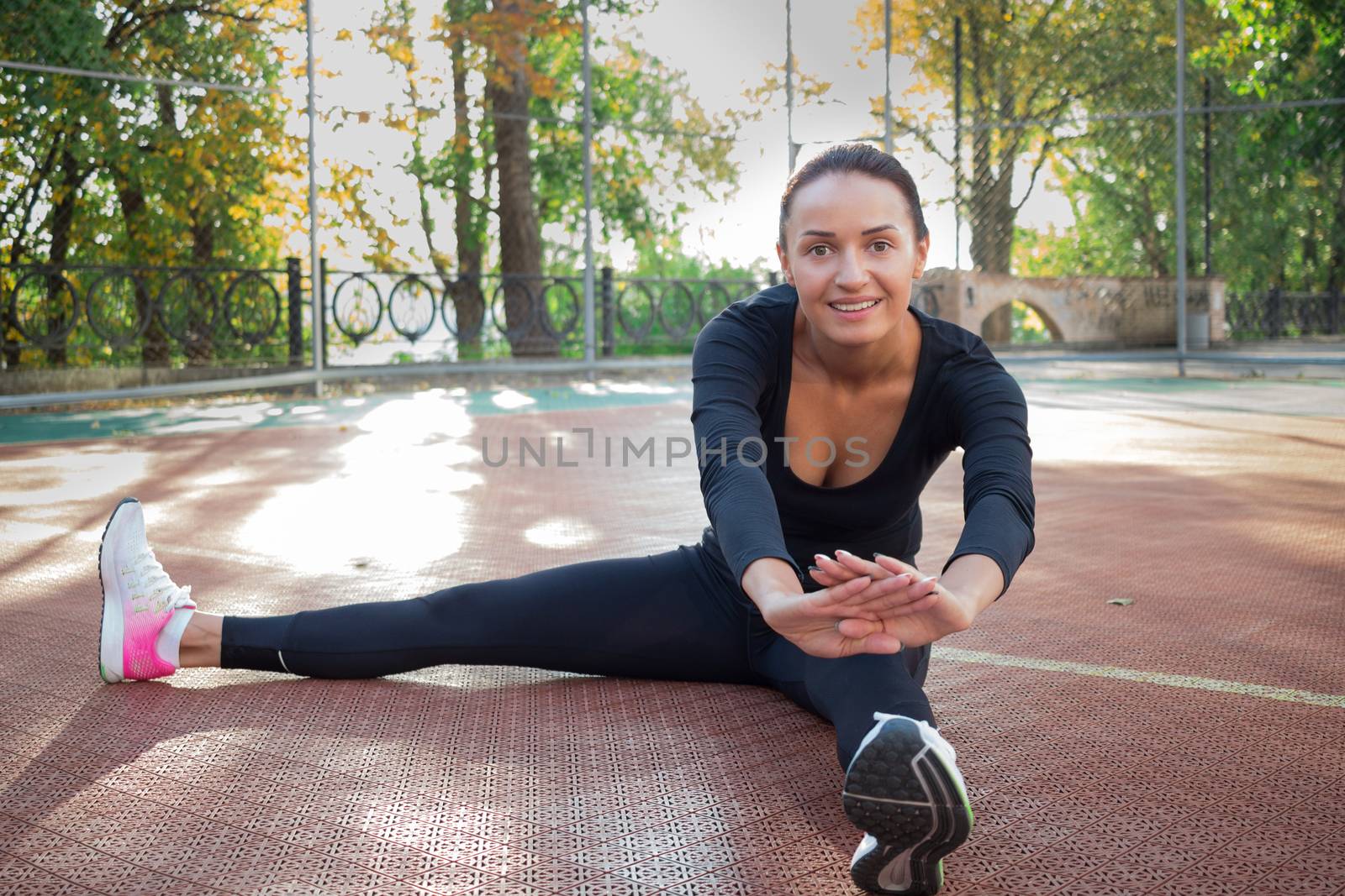 Young pretty fitness woman does stretching exercises during sport training workout on playground outdoor