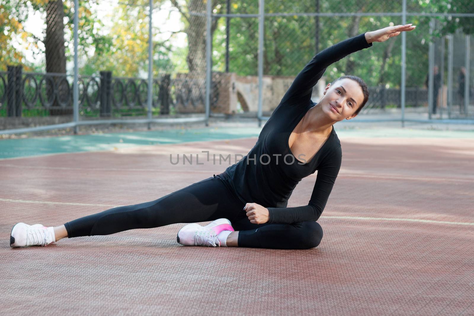 Young pretty fitness woman does stretching exercises during sport training workout on playground outdoor